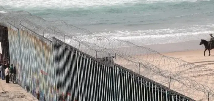 people watch as a mounted U.S. border agent patrols along the beach by the wall separating the U.S. and Mexico on January 28, 2019 in Tijuana